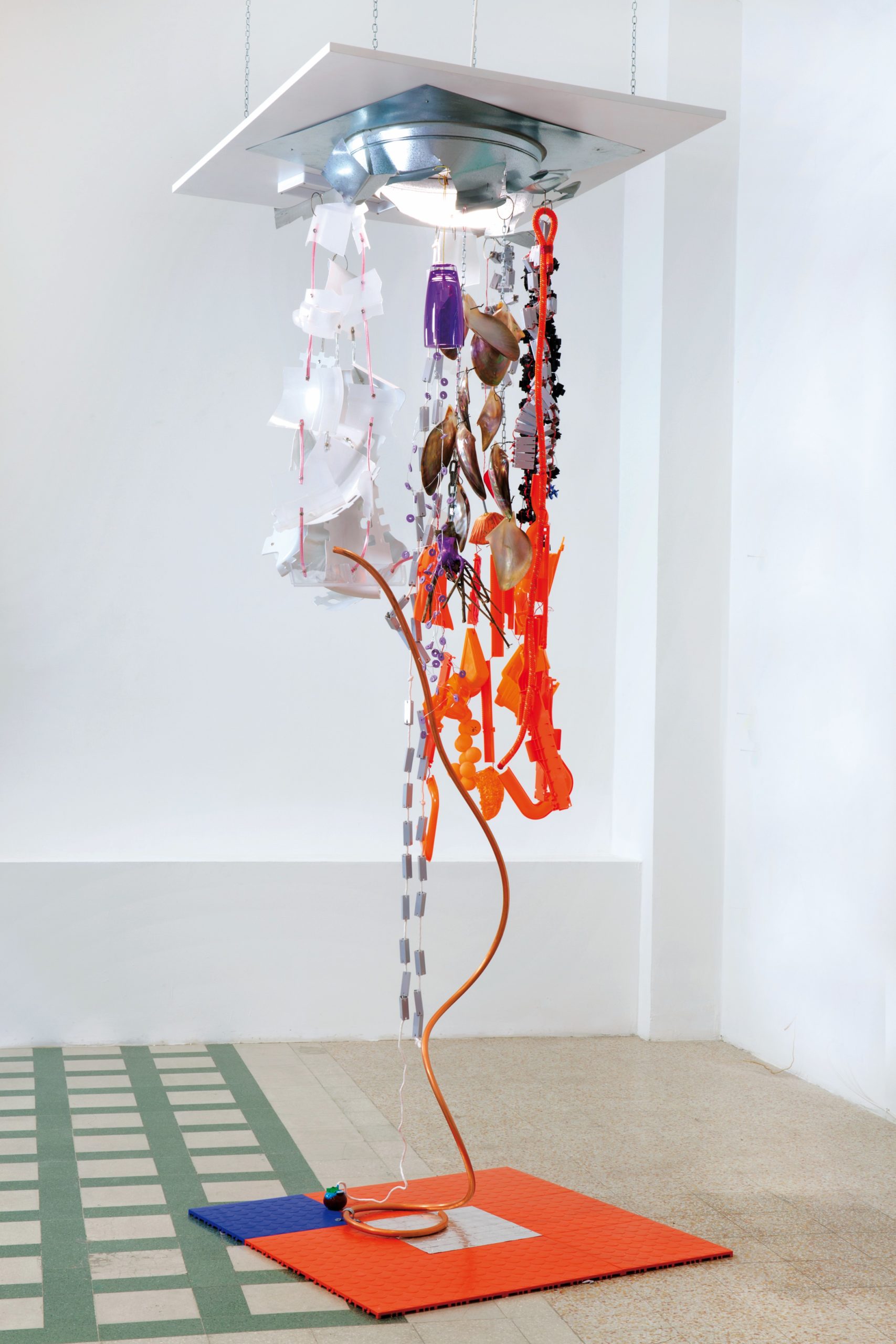 Draft, 2014
Plastic garage floor tiles, copper tubing, foil, wooden pepper mill part, acrylic paint, plastic parts, electric cord, wooden branch, rubber washers, wire, shells, galvanized steel vent part, white metal bracket, orange rope, white rope, zip ties, key chain wires, orange ping pong balls, rubber, rivets. Light fixture: recessed LED ceiling fixture. 
116,8 × 91,4 × 91,4 cm. 
Jessica Stockholder
courtesy of the Artist and Galleria Raffaella Cortese, Milano 
Foto: Lorenzo Palmieri